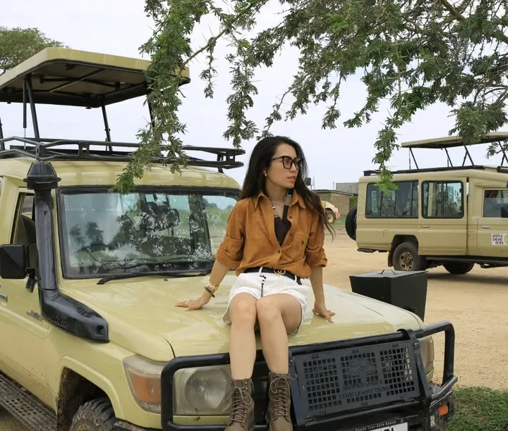 Safari guest sitting on the bonnet of a safari vehicle, smiling at the camera