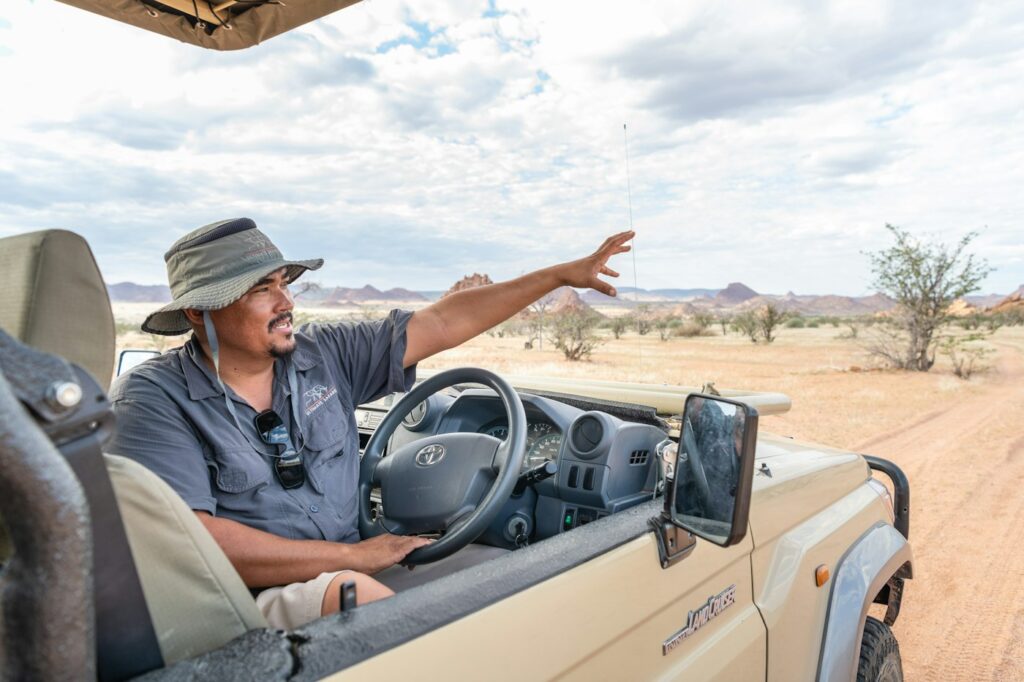 Safari guide at the wheel of an open vehicle pointing out the view